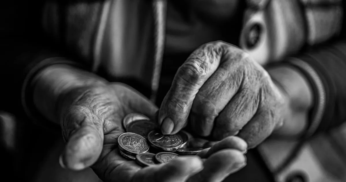 Mãos de uma pessoa idosa segurando um punhado de moedas, em preto e branco